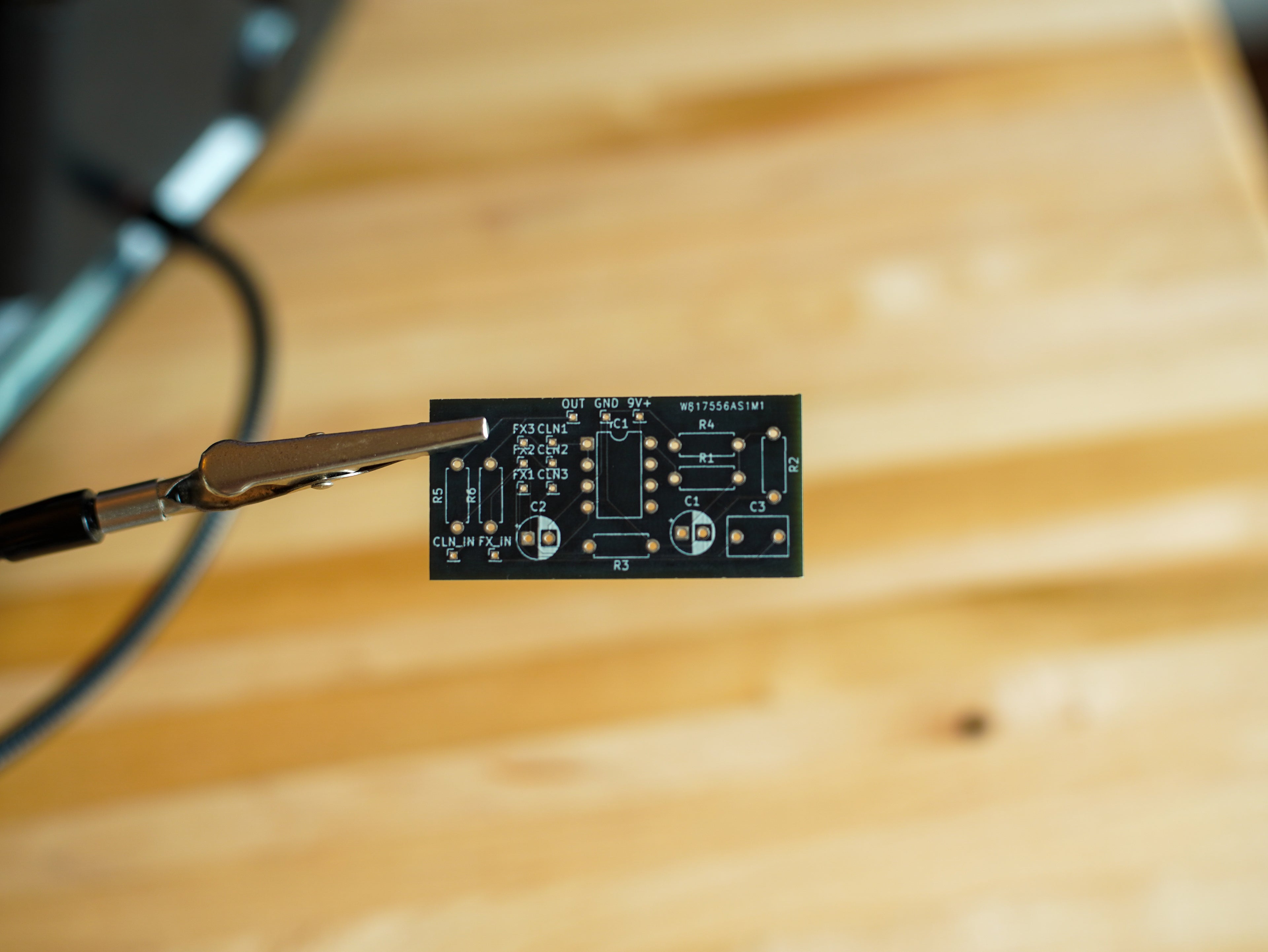 Small electronic circuit board held by tweezers on a wooden surface