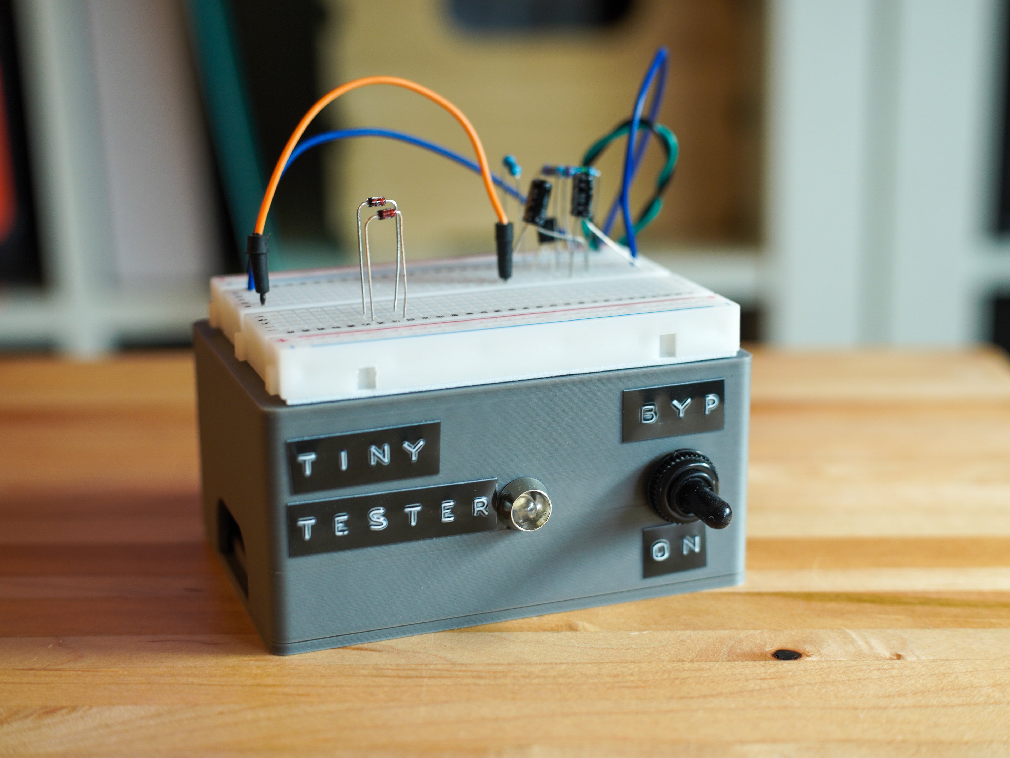 Electronic device labeled 'Tiny Tester' on a wooden surface